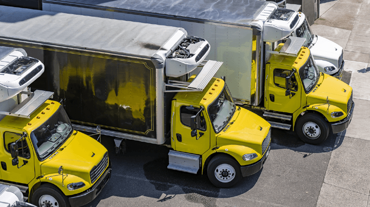 Several yellow refrigerated trucks featuring JEAR Logistics are parked side by side at a loading dock, viewed from above.