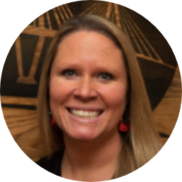 A woman with long blonde hair, wearing red earrings, smiles at the camera. The background features a wooden design with geometric lines and shapes, creating a modern atmosphere reminiscent of JEAR Logistics contemporary style.